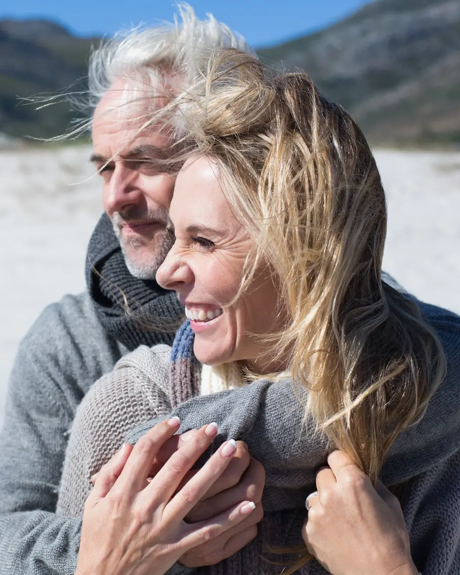 A couple on a windswept beach, wrapped up warm and smiling