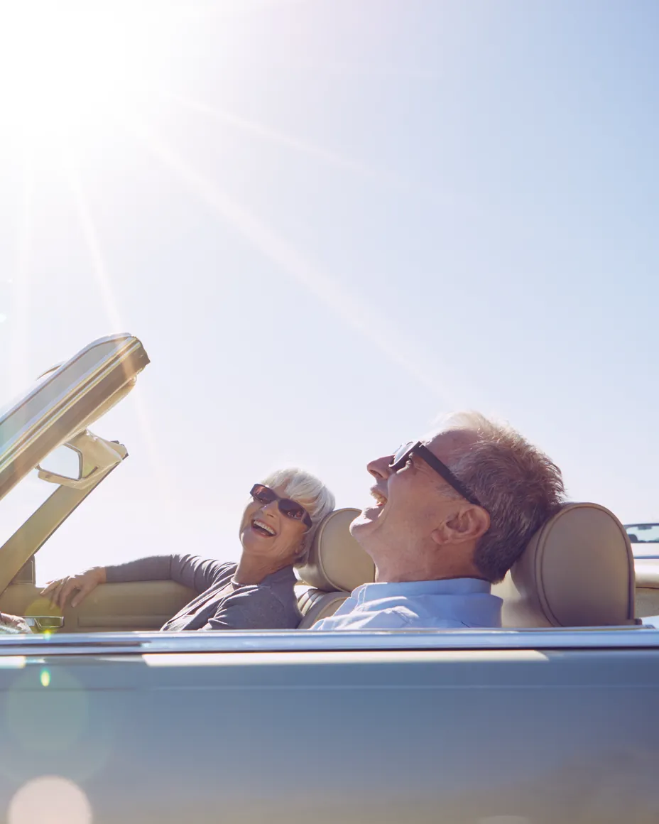 A couple laughing in an open-top car on a bright day